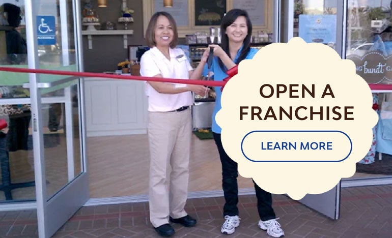 Two individuals outside the Bakery cutting a ribbon. Open a Franchise. Learn more.